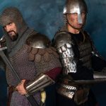 Two knights in full plate and chainmail armor pose with swords, standing side by side against a dark blue backdrop.